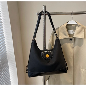 Detail of black canvas and patent leather tote bag hanging on a metal hanger in sunlight