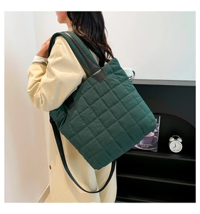 Model wearing dark green quilted nylon tote bag with crossbody strap and beige coat