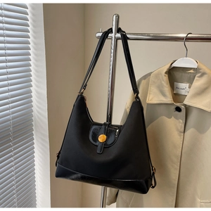 Detail of black underarm tote bag with sleek curved design and gold buckle accent