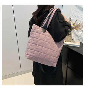 Detailed view of light pink quilted tote bag with black strap worn by a model