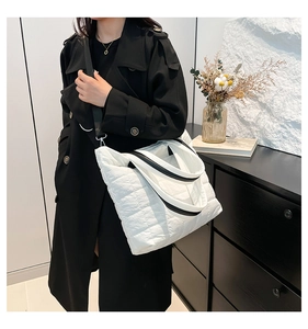 Detail of white quilted tote bag featuring black and white striped straps and soft texture