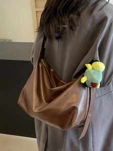 Brown large capacity pleated hobo shoulder bag with a turtle charm worn by a model