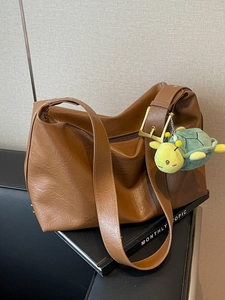 Large brown leather tote bag with wide shoulder strap and green turtle plush accessory