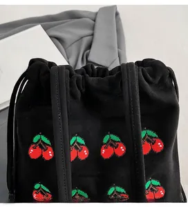 Detail of cherry embroidery on black suede drawstring bucket bag with dual ribbon handles