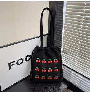 Detailed macro view of black canvas bucket bag featuring red cherry embroidery and drawstrings