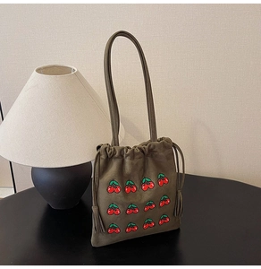 Detail of army green bucket bag featuring cherry embroidery and tassel drawstring detail