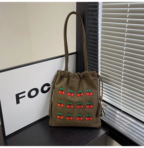 Detail of olive green suede bucket bag featuring red cherry embroidery and tassels