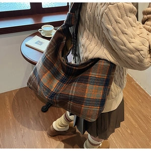 Detail shot of a large wool-textured plaid tote bag styled in a cozy cafe setting