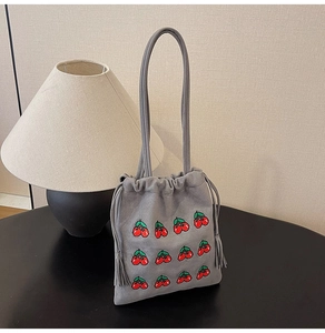 Detail of grey suede bucket bag featuring embroidered red cherries and side tassels
