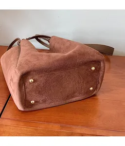 Détail d'un sac seau en daim marron avec des pieds de protection dorés sur le fond