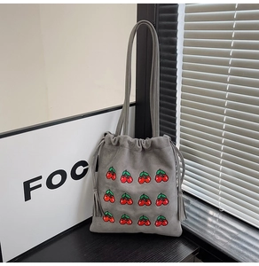 Detail of grey suede bucket bag featuring red cherry embroidery and tassel drawstring
