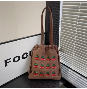 Detail of cherry embroidery on brown faux suede bucket bag with drawstring and tassel