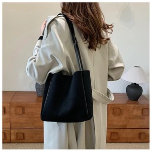 Détail d'un élégant sac cabas en cuir mat noir porté avec un trench-coat beige