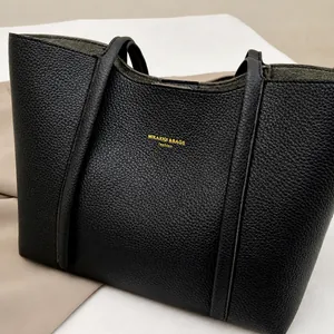 Detalle del bolso tote de cuero granulado negro con logotipo dorado y correas anchas
