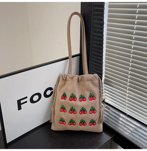 Detail of khaki drawstring tote bag featuring red cherry embroidery and tassel charms