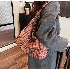 Detail of red and orange plaid hobo bag featuring decorative knot strap and thick woolen texture