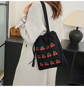 Detail of embroidered cherry patterns and tassels on a black canvas drawstring bucket bag