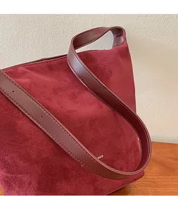 Detail of the adjustable leather shoulder strap and burgundy frosted suede texture on the bag