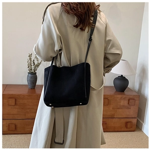 Détail d'un sac seau noir en PU avec des rivets dorés porté par un mannequin