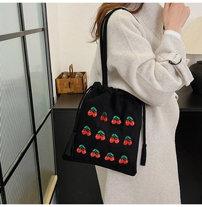 Detail of black canvas drawstring bucket bag with red cherry embroidery and tassels