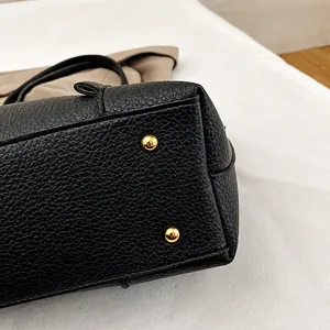 Detalle de bolso tote de cuero negro con remaches protectores de metal dorado en la base