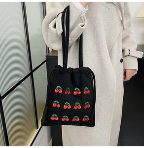 Detail of black canvas bucket bag featuring red cherry embroidery and drawstring closure