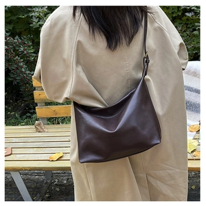 Deep brown minimalist half-moon bag worn with a khaki trench coat in an outdoor park setting