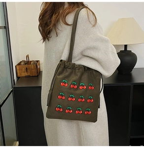 Detail of dark olive green bucket bag featuring red cherry embroidery and tassel drawstring