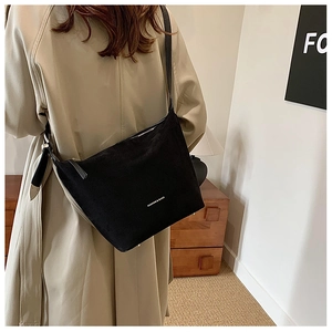 Detailed view of black matte bucket bag with white fashion text on khaki trench coat