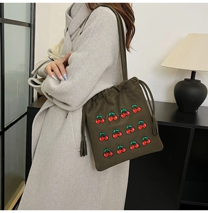 Close-up of olive green bucket bag featuring red cherry embroidery and tassel drawstring