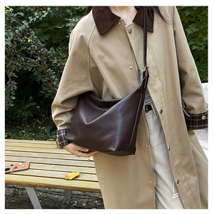 Detail of dark brown leather crossbody bag styled with a khaki trench coat outdoors