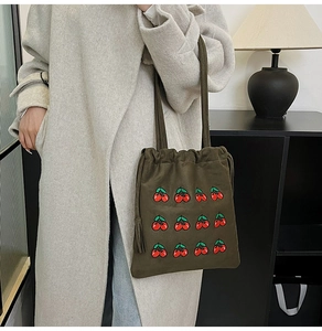 Detail of dark olive green suede bucket bag with red cherry embroidery and drawstring