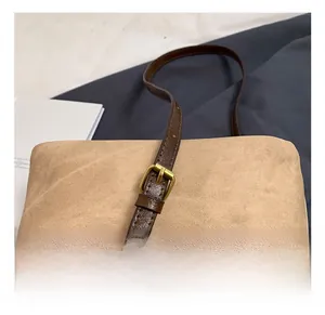 Détail de la bandoulière réglable en cuir marron foncé avec boucle dorée sur un sac en toile