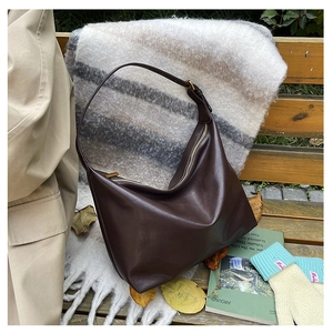 Deep brown leather dumpling bag displayed on a wooden bench with autumn accessories