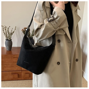 Close-up of matte black PU leather crescent shoulder bag paired with a classic trench coat