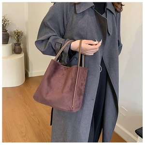 Détail du sac seau en daim marron avec poignées en cuir pour une tenue d'automne