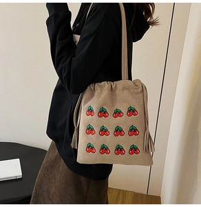Detail of drawstring bucket bag with red cherry embroidery and tassel charms on shoulder