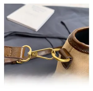 Détail des crochets dorés et des lanières en cuir marron sur un sac seau en toile