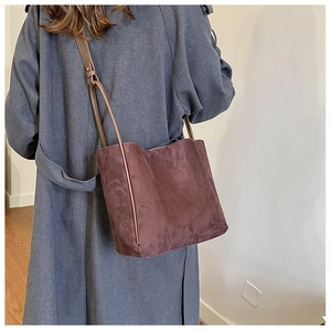 Détail d'un sac seau en daim bordeaux avec bandoulière en cuir marron sur modèle
