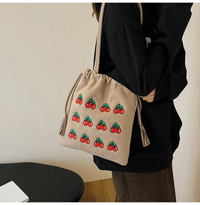 Detail of embroidered cherry patterns on beige faux suede drawstring bucket bag with tassels