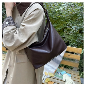 Brown retro large shoulder bag styled with a long trench coat in an autumn outdoor park