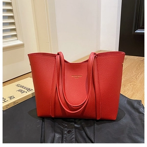 Detalle del bolso tote de cuero granulado rojo con logo dorado y correas de hombro finas