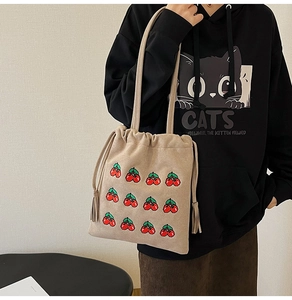 Detail of embroidered cherry patterns and drawstring tassels on the beige tote bag