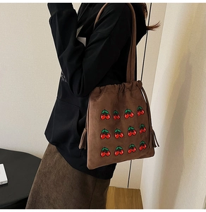 Detail of brown suede bucket bag with cherry embroidery and tassel drawstring closure