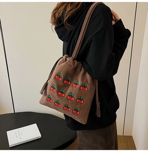 Brown suede bucket bag featuring detailed red cherry embroidery and tassel drawstring detail