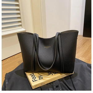 Detalle del bolso tote de cuero lichi negro con elegantes letras doradas del logo frontal