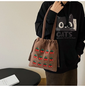 Close-up of brown suede bucket bag featuring red cherry embroidery and drawstring tassels
