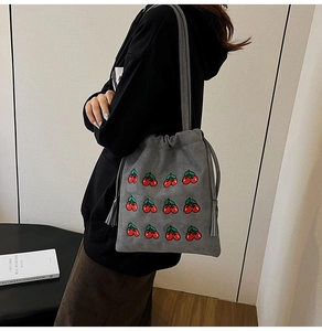 Close-up of gray drawstring bucket bag featuring red cherry prints and tassel details