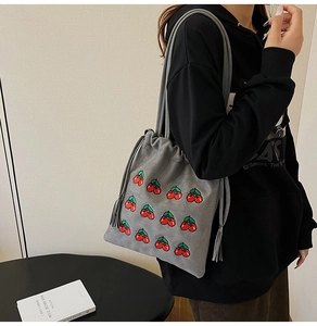Close-up of gray drawstring tote bag with red cherry embroidery on soft fabric