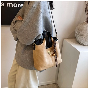 Détail d'un sac cabas en daim kaki avec bordures en cuir noir et breloque décorative